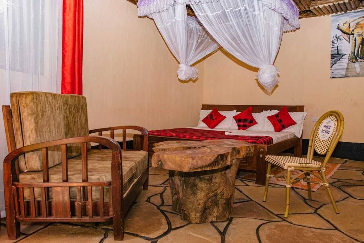 Una habitación con una cama, dos sillas de madera, una mesita y una silla con un cartel.