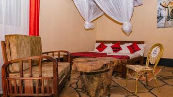 Una habitación con una cama, dos sillas de madera, una mesita y una silla con un cartel.