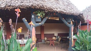 Un restaurant en plein air, doté d’un toit de chaume, de mobilier en bois et d’une enseigne indiquant qu’il s’agit d’un restaurant.