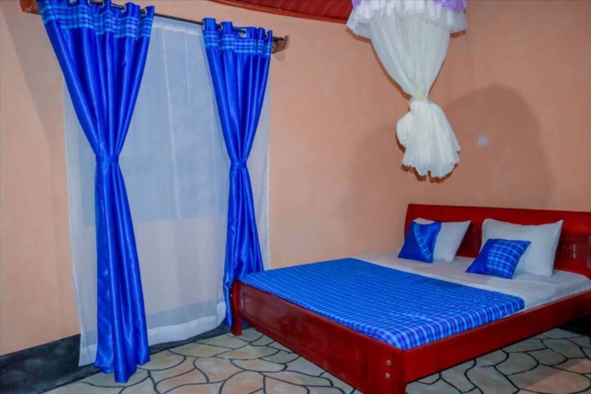 Un dormitorio con estructura de cama roja, colcha azul y dos almohadas. Hay una ventana con cortinas azules y un dosel blanco.