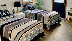Quarto com duas camas, uma janela com persianas, um relógio na parede e uma porta.