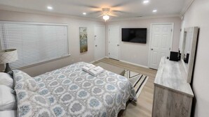 Un dormitorio con cama, televisión, cómoda y ventilador de techo.