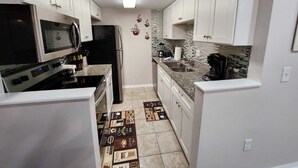 Una cocina compacta con armarios blancos, microondas, refrigerador y cafetera.