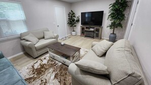 Una sala de estar con un sofá, una mesa de centro, un televisor y dos plantas en macetas.