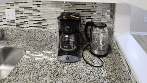 Una cocina con cafetera, hervidor y un armario con repisa.