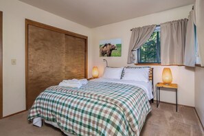 A bedroom with a bed, two bedside lamps, a window with curtains, a door, and a wall-mounted picture.