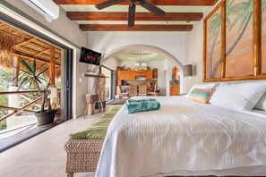 A bedroom with a large bed, a TV mounted on the wall, and a view of the outside.