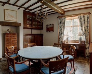 A dining room with a round table, wooden chairs, a chandelier, and a window with curtains.