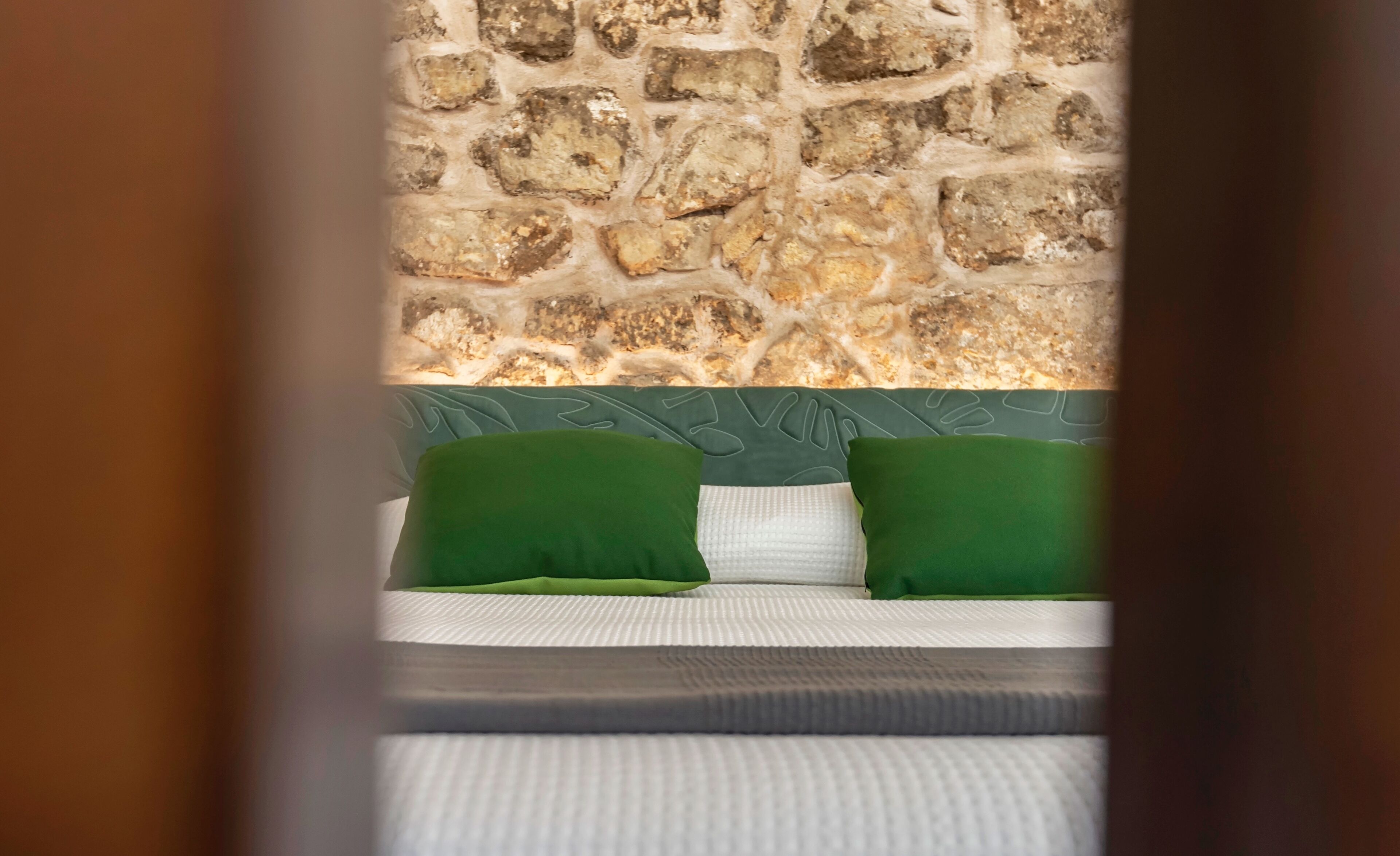 A bed with green pillows and a stone wall behind it.