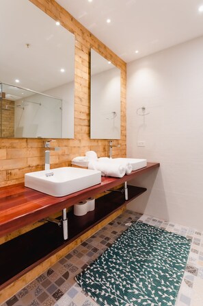 A modern bathroom with a wooden vanity, two sinks, a large mirror, and a patterned rug.