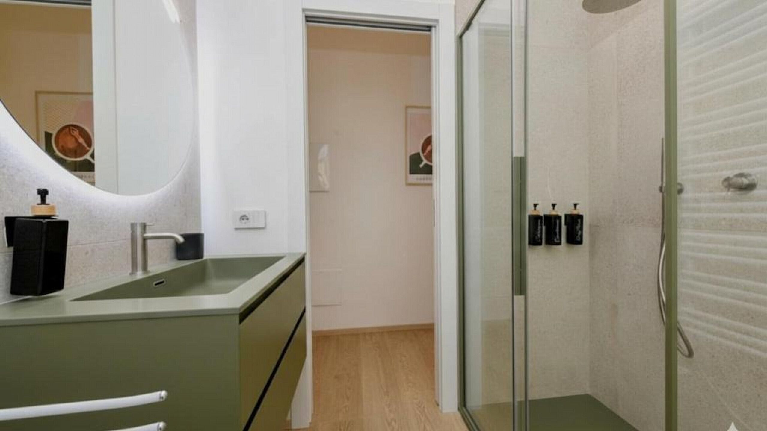 A modern bathroom with a glass shower enclosure, a sink with a mirror, and two soap dispensers on the wall.