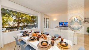 Un comedor con una mesa dispuesta para una comida, un televisor en la pared y vistas a árboles y edificios.