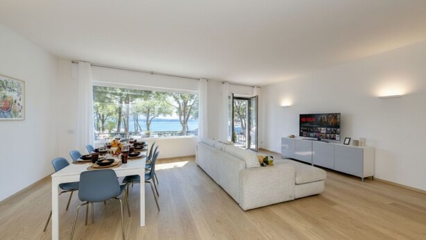 Una sala de estar moderna con comedor, ventanas amplias, un sofá blanco y un televisor.