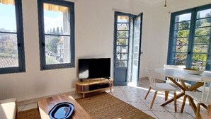 A living room with a TV, a dining table with chairs, and large windows with shutters. - Bright Appartment, perfect location (Saint-Jean-Cap-Ferrat)