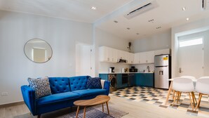 A modern apartment with a living area featuring a blue sofa, a round mirror, and a wooden coffee table. The kitchen has a checkered floor and white cabinets. - Casa Love 3A (Panama City)