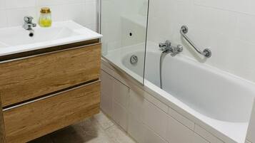 A bathroom with a white sink, wooden vanity, and a glass-enclosed bathtub with a showerhead.