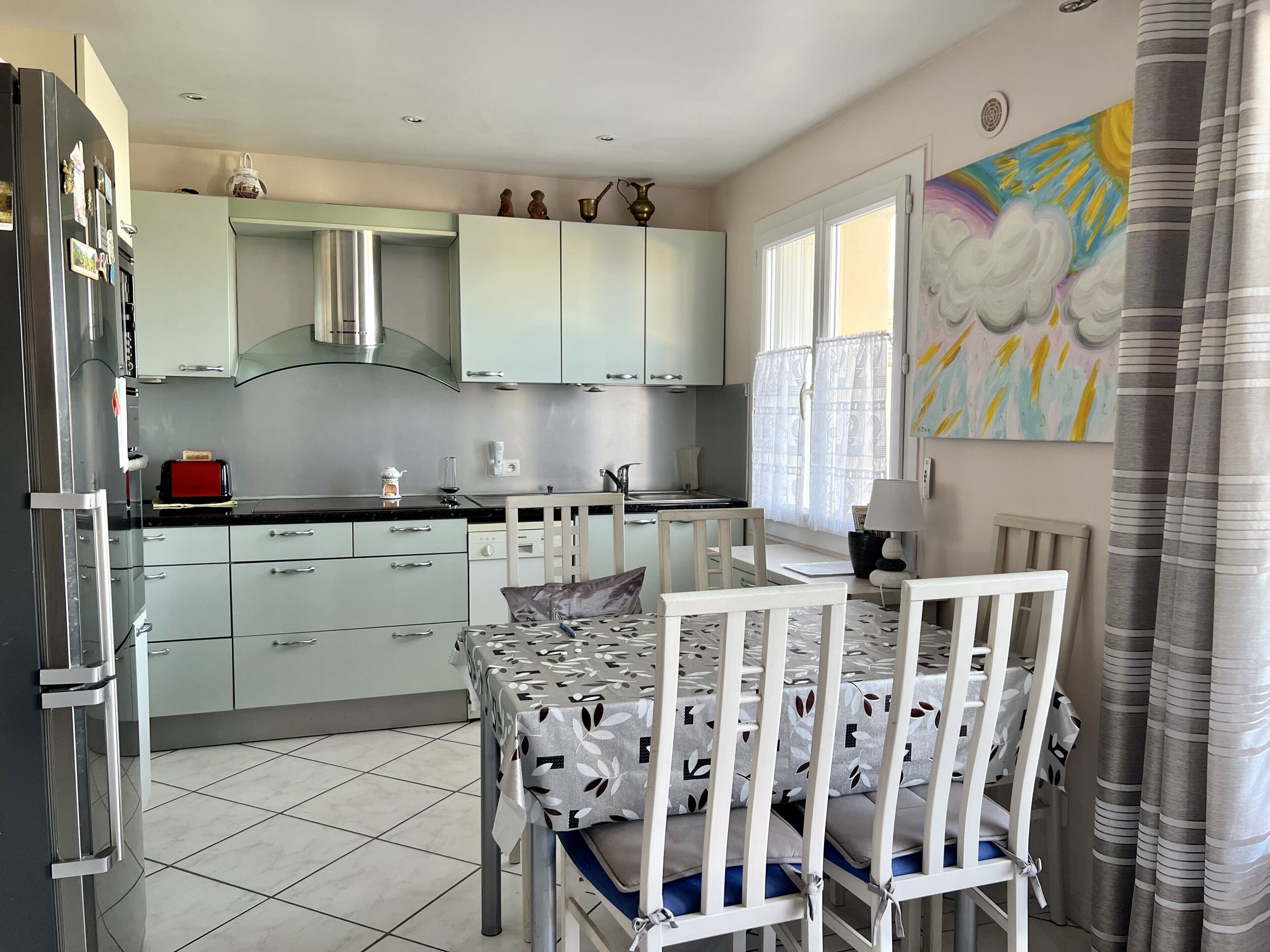 A modern kitchen with light green cabinets, a red toaster, and a dining table with white chairs.