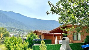 Una cabaña de madera con techo de tejas, rodeada de follaje cuidado y vistas a un paisaje montañoso.