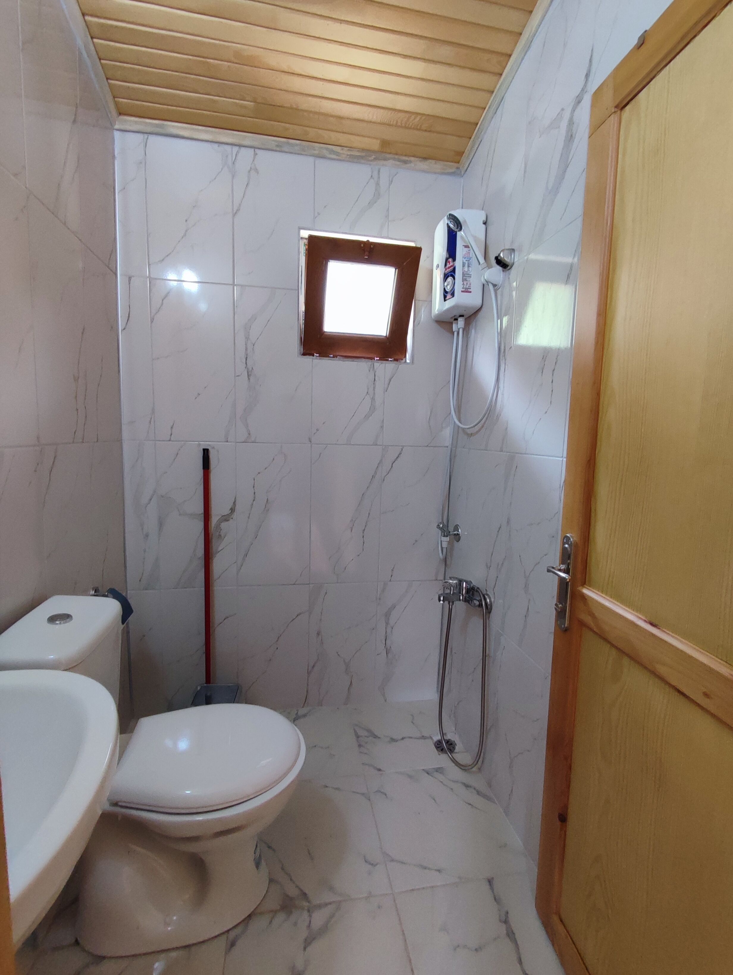 A bathroom with a toilet, a shower, and a small window.