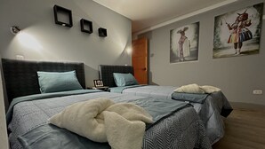 Een slaapkamer met twee bedden, elk voorzien van beddengoed en kussens met een patroon. Er hangen foto's in lijsten aan de muur en er is een schilderij.
