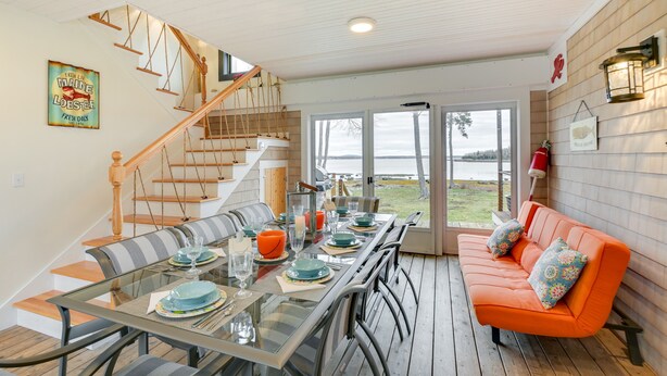A dining area with a glass table, striped cushions, and a wooden staircase. - Waterfront Deer Isle Apartment w/ Fire Pit (Deer Isle)