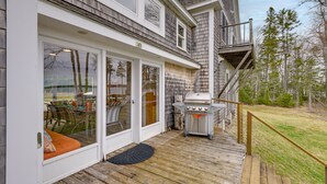 A covered patio with a grill, a sliding glass door, and a deck with outdoor furniture. - Waterfront Deer Isle Apartment w/ Fire Pit (Deer Isle)