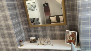 A bathroom with a checkered tile wall, a mirror with a gold frame, a vanity with a white countertop, and a framed picture on the wall.
