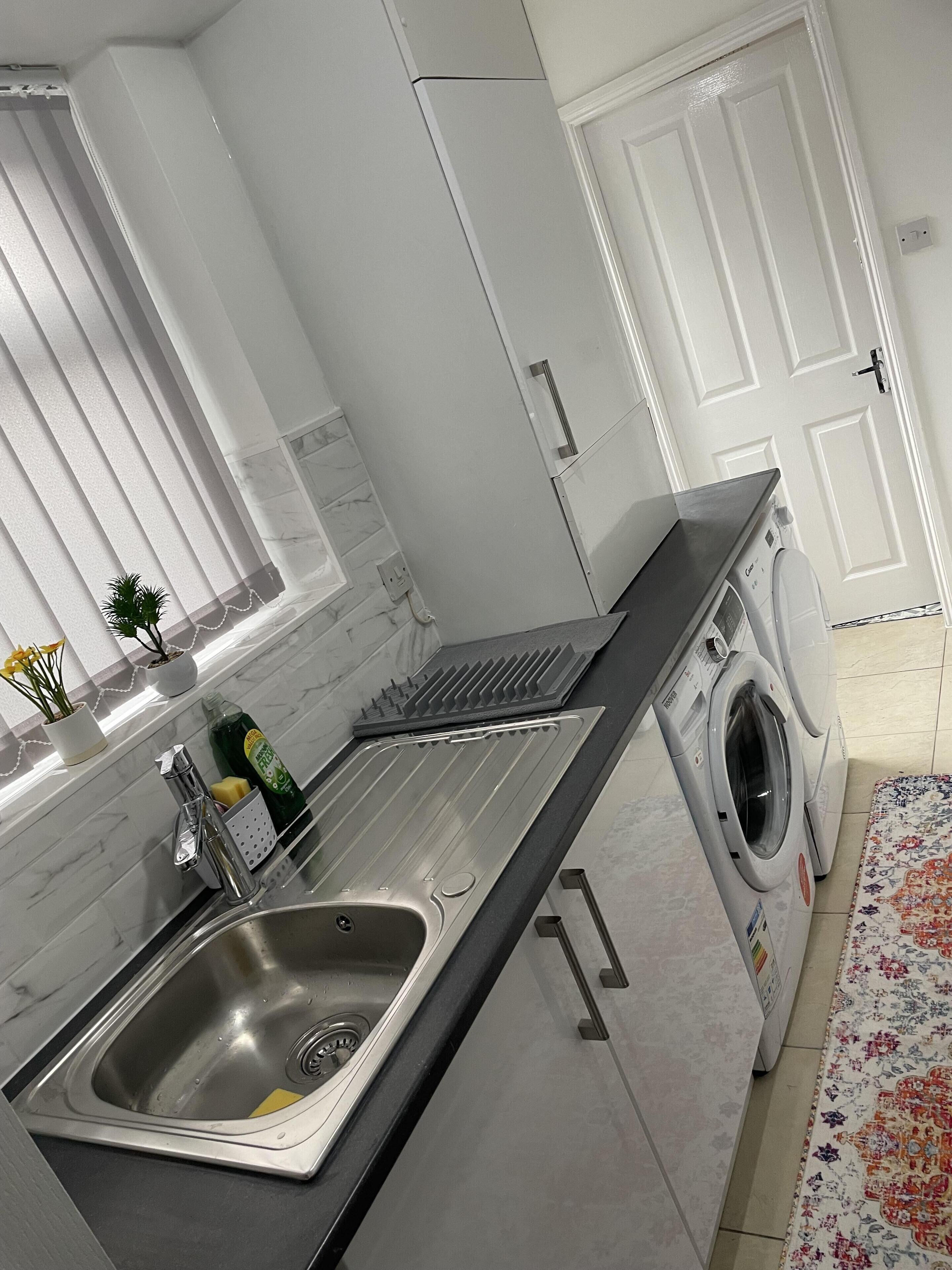 A modern kitchen with a stainless steel sink, a built-in washing machine, and a marble backsplash.