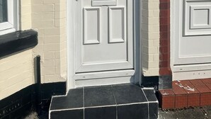 A white door with the number 8, flanked by two windows, one with a red brick wall and the other with a white wall.