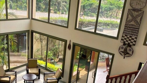A spacious room with large windows offering views of a lush garden. There are several chairs and a small table, and a staircase is visible in the foreground. - Veronica Guest House (Lomé)