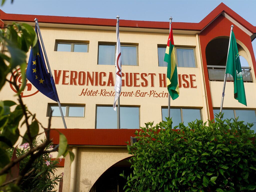 The Veronica Guest House building with multiple flags, including the European Union flag, and a sign indicating it offers hotel, restaurant, bar, and pool services.