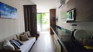 A modern living room with a sofa, a television, and a kitchen area with a blender.