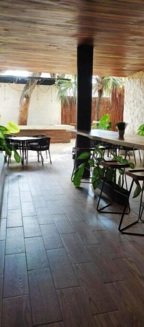 A spacious indoor area with a long table and chairs, surrounded by potted plants and a stone wall. - Veleros II (Tulum)