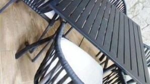 A round black metal table with four chairs, a potted plant, and a stone wall in the background.