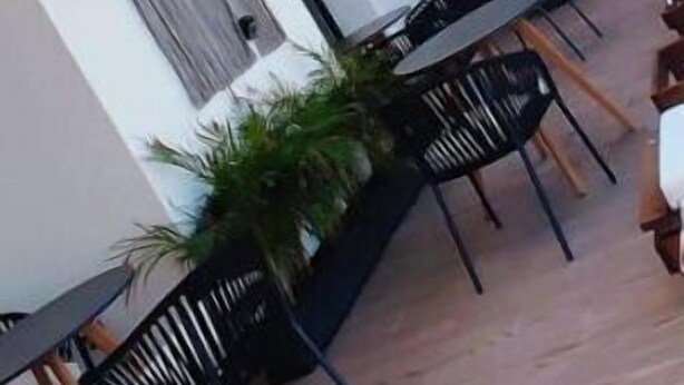 An outdoor patio area with tables and chairs, a pergola with hanging baskets, and a white building with a window and a door.