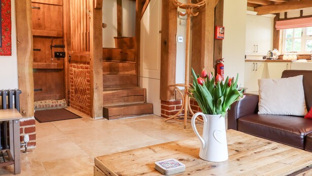 Un escalier en bois mène à une chambre à coucher située en mezzanine, un coin repas avec une table et des chaises, et une cuisine à l’arrière-plan.
