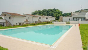 A swimming pool with a tiled deck, surrounded by modern buildings with stone accents and a grassy area.
