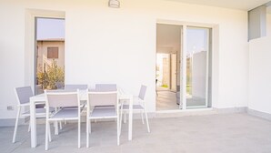 A modern patio with a white table and chairs, a glass door leading to a garden, and a clear view of the outside.