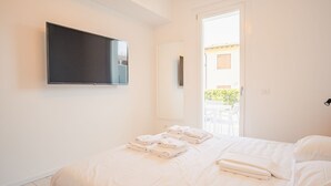 A hotel room with a bed, a flat-screen TV mounted on the wall, and a door leading to an outdoor area with a table and chairs.