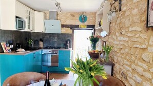 A kitchen with a stone wall, a dining table set with food and drinks, and a view of the outside. - Charming cottage within a perigordine farmhouse  (Saint-Cyprien)