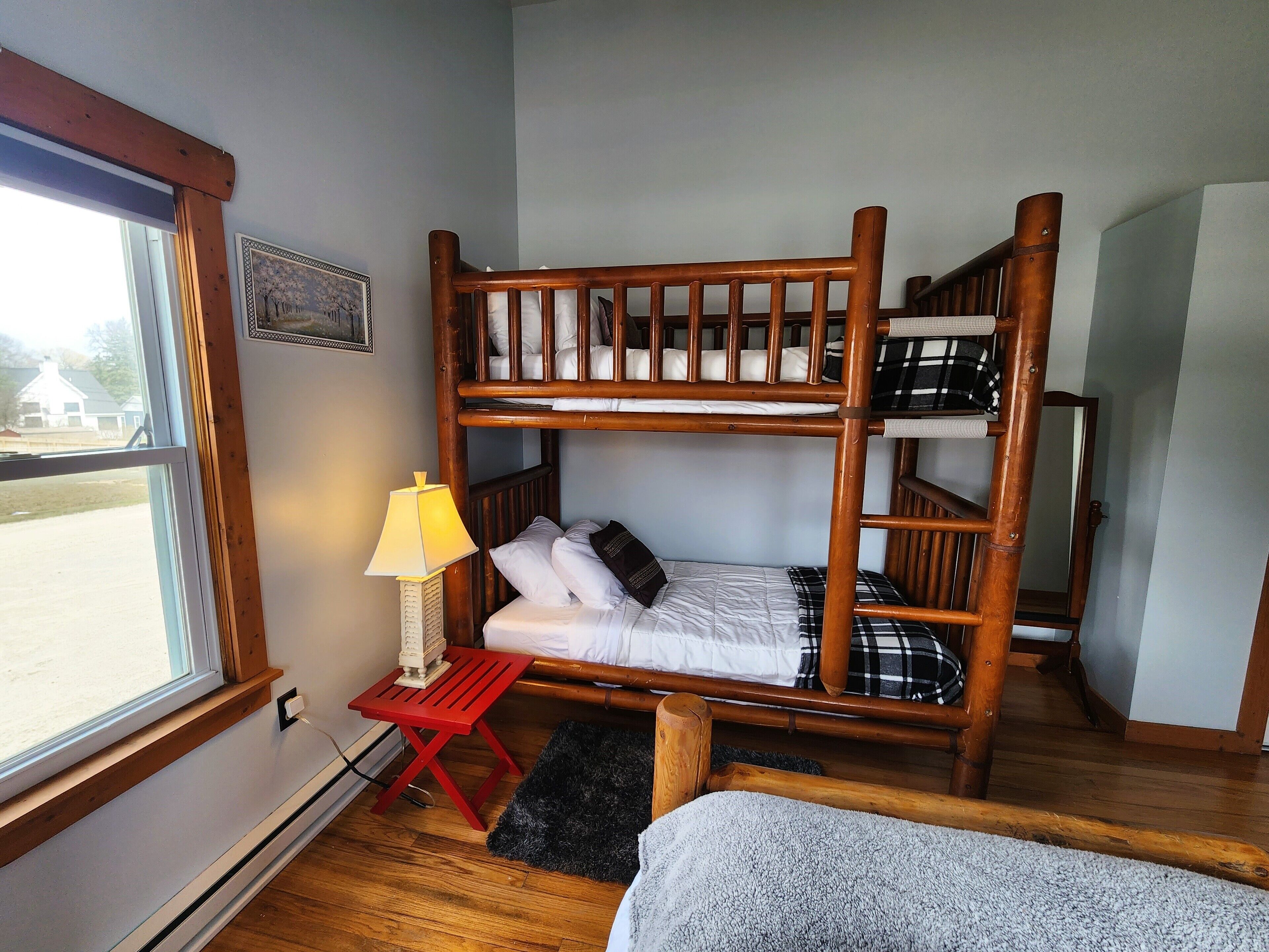 A bunk bed room with a window, a red table with a lamp, and a black rug.
