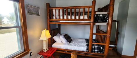 A bunk bed room with a window, a red table with a lamp, and a black rug.