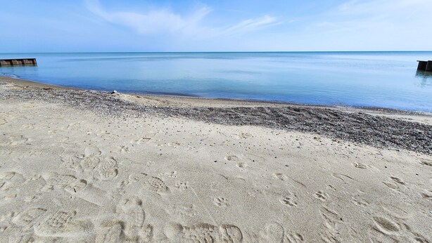 Une plage avec un ciel dégagé, une eau calme et un rivage de galets.
