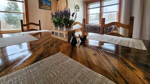 Un coin repas avec une table en bois, quatre chaises, un vase de fleurs et une fenêtre avec des stores.