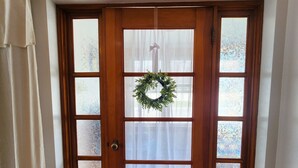 Une porte d’entrée en bois avec des panneaux de verre dépoli, une guirlande accrochée au-dessus, et un rideau blanc sur le côté gauche.