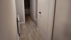 A narrow hallway with a white door on the right, a radiator on the left, and a ceiling light. - Beautiful 2-bed Apartment in London - Sleeps 6! (London)