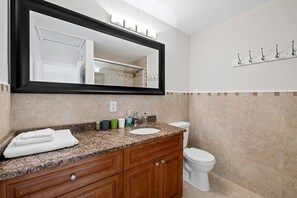 Un baño con encimera de granito, un lavamanos blanco, un espejo, un inodoro y un perchero para toallas.