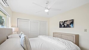 A bedroom with a bed, a ceiling fan, a window, and a wall-mounted artwork. - Bermuda Isles Villas - King #29 (Lauderdale-by-the-Sea)