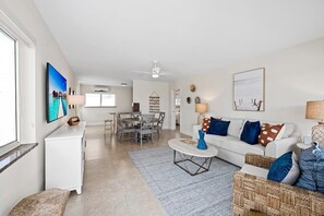 Een ruime woonkamer met een witte bank, een salontafel en een eethoek met een tafel en stoelen.