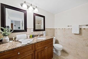 A bathroom with a granite countertop, wooden vanity, two mirrors, a white toilet, and a towel rack.